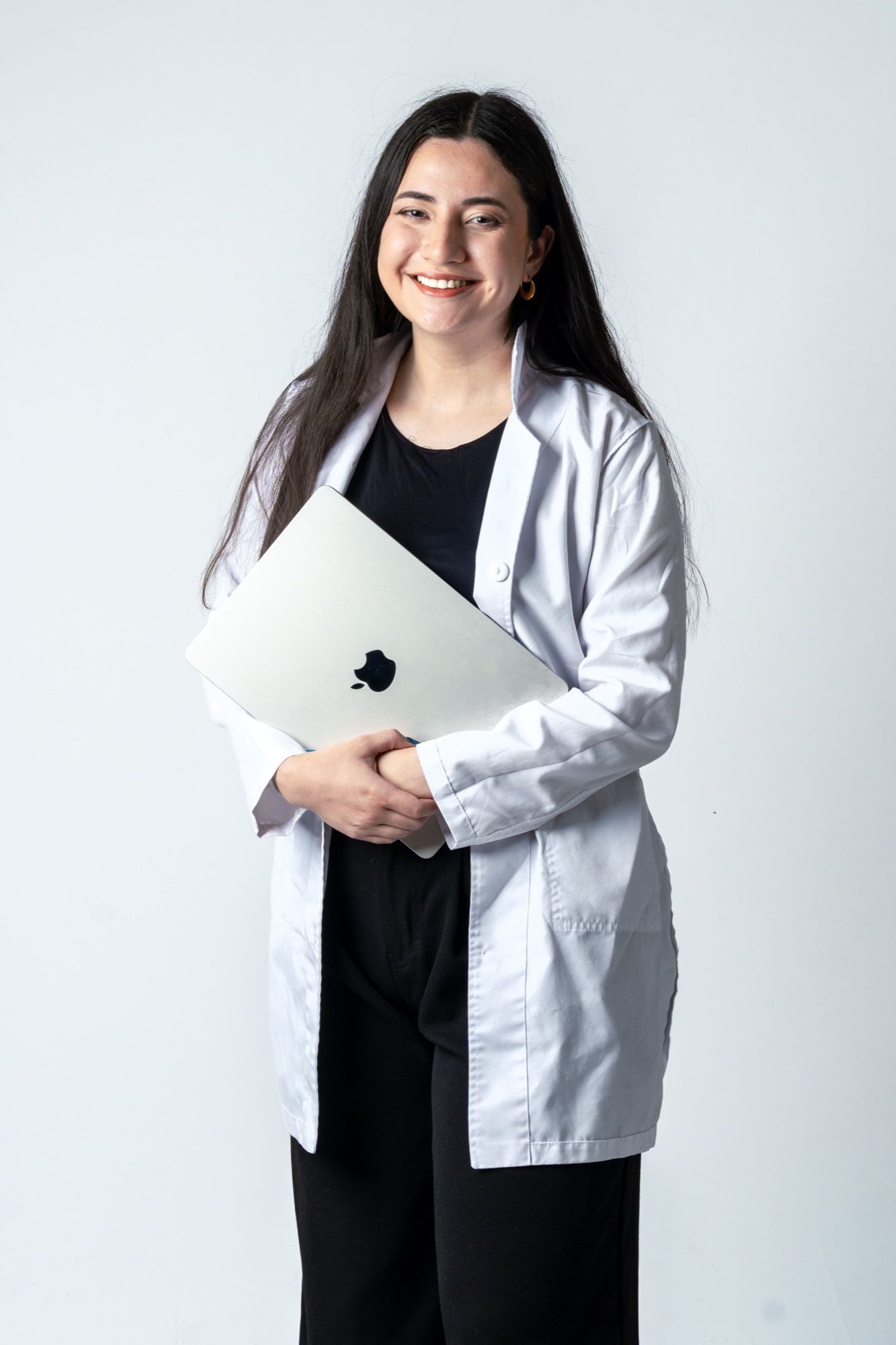 Angie Paladines con bata blanca sostiene una laptop y sonríe